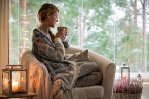 woman-curled-up-in-blanket-on-chair-and-hot-beverage-looking-out-window