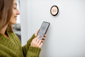 thermostat-on-wall-with-celsius-reading-and-woman-using-smartphone