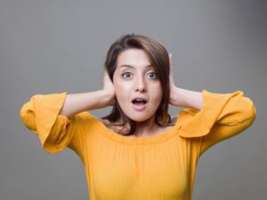 Young woman in a yellow blouse covering her ears and looking surprised