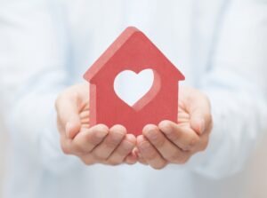 Small red house with heart in hands 